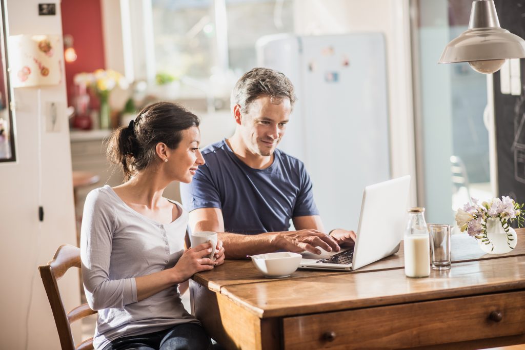 Couple booking holiday on laptop, sat at table